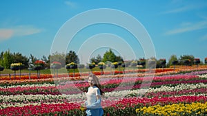 Happy girl running on floral background outdoors. Young woman in tulip field.