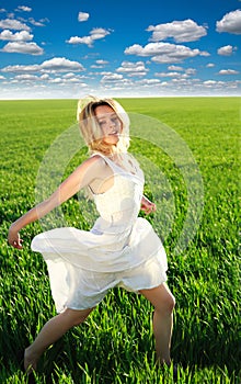 Happy girl running on the green blossoming field under blue sky