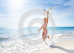 Happy girl runs at the beach and holds toy plane