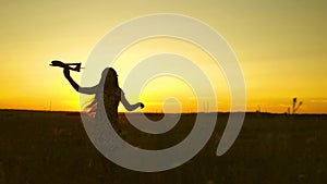 Happy girl runs with a toy airplane on a field in the sunset light. children play toy airplane. teenager dreams of