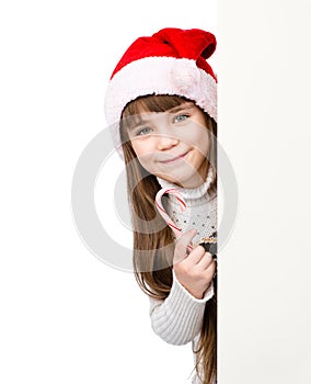 Happy girl in santa hat with Christmas candy cane standing behind banner on white