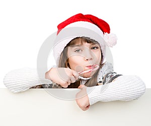 Happy girl in santa hat with Christmas candy cane standing behind white banner. isolated on white