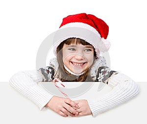 Happy girl in santa hat with Christmas candy cane standing behind white board. isolated on white background