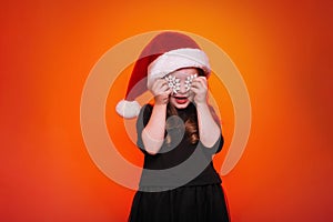 Happy girl in santa hat with christmas toys on red background. Funny young child waiting for christmas, new year and presents.