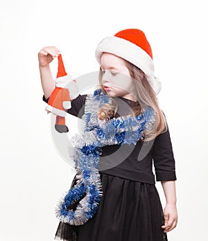 Happy girl in santa hat with christmas toys on white background. Funny young child waiting for christmas, new year and presents.