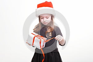 Happy girl in santa hat with gift on white background. Funny young child waiting for christmas, new year and presents. holiday,