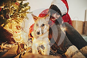 Happy girl in santa hat hugging with cute dog on background of g