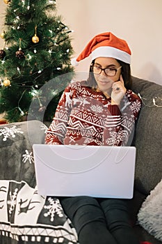 Happy girl with Santa hat looking for presents on laptop