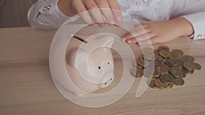 Happy girl save money in piggy bank in her home. Child inserting a coin into a piggy bank, indoor financial concept. Kid