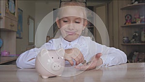 Happy girl save money in piggy bank in her home. Child inserting a coin into a piggy bank, indoor financial concept. Kid