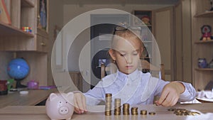 Happy girl save money in piggy bank in her home. Child inserting a coin into a piggy bank, indoor financial concept. Kid