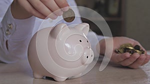 Happy girl save money in piggy bank in her home. Child inserting a coin into a piggy bank, indoor financial concept. Kid