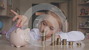 Happy girl save money in piggy bank in her home. Child inserting a coin into a piggy bank, indoor financial concept. Kid