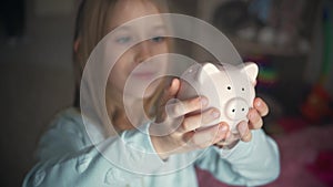 Happy girl save money in piggy bank in her home. Child inserting a coin into a piggy bank, indoor financial concept. Kid