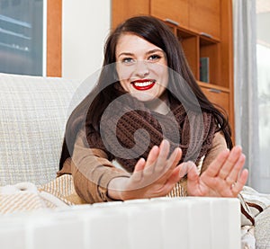 Happy girl in scarf warming near warm heater