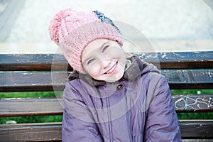 Happy girl-schooler sitting on bench in city park.