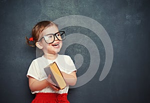 Happy girl schoolgirl with book from blackboard