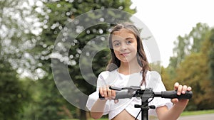 A happy girl on a scooter, smiling, enjoying outdoor recreation under the sky.