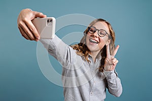 Happy girl showing peace sign while taking selfie on cellphone