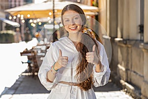 Happy girl showing thumbs up, like sign positive something good positive feedback in city street