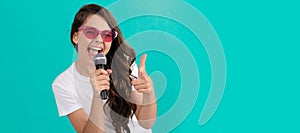 Happy girl singer point finger gun singing song to microphone blue background, karaoke. Horizontal poster of isolated