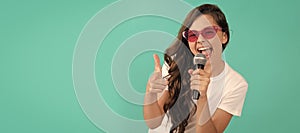 Happy girl singer point finger gun singing song to microphone blue background, karaoke. Horizontal poster of isolated