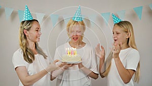 happy girl with sister and mom celebrate birthday by blowing out candles on cake and clapping hands