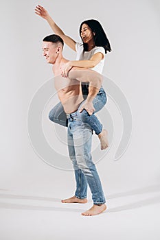 A happy girl is sitting on the back of her boyfriend, they are dancing and having fun. Beautiful woman jumps in arms of