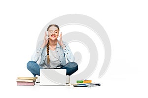 Happy girl sitting on floor in headphones near laptop, books and copybooks