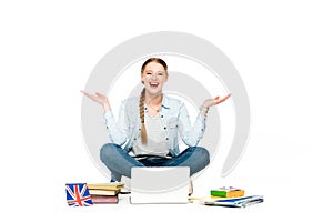 Happy girl sitting on floor with laptop, books and copybooks, uk flag and gesturing