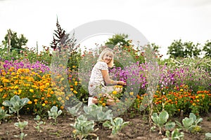 Happy girl sitting on a flower bed near the cabbage in the garden in a country house and posing for the camera with a smile on his