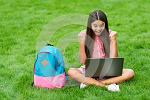 Happy girl sitting on green grass with laptop. Start up. child playing computer game. back to school. education online