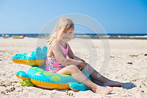 Happy girl sitting on an inflatable crocodile toy at the beach sunny day