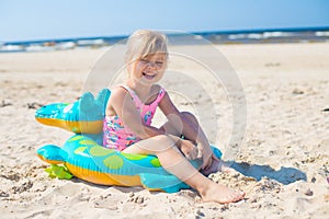 Happy girl sitting and laughing on an inflatable crocodile toy at the beach sunny day
