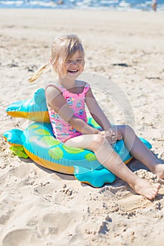 Happy girl sitting and laughing on an inflatable crocodile toy at the beach sunny day