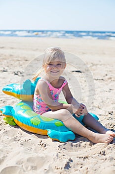 Happy girl sitting and laughing on an inflatable crocodile toy at the beach sunny day