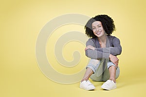 Happy girl sitting smiling on yellow background with copy space.