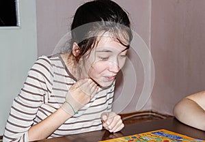 A happy Girl is sitting at a table in a room and playing a Board game