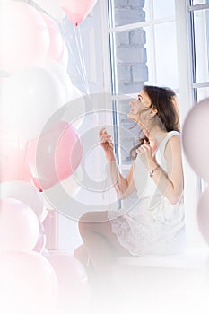 Happy girl sitting on a windowsill with balloons