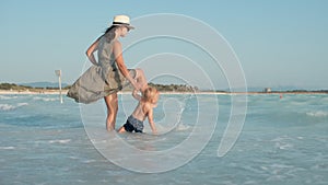 Happy girl with son playing at coastline. Baby boy with mother going to water.