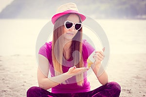 Happy girl in straw hat and sunglasses using sun lotion, sun protection on beach