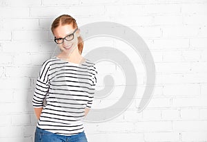 Happy girl student in glasses at a blank white brick wall