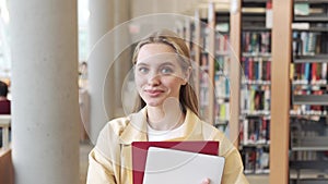 Happy girl student holding notebooks standing in university library, portrait.