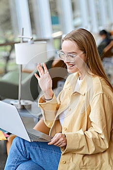 Happy girl student waving hand looking at laptop hybrid learning. Vertical