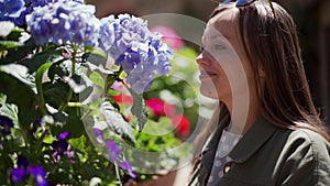 Happy girl with sunglasses looks at blue hydrangeas and smells flower. Sunny day