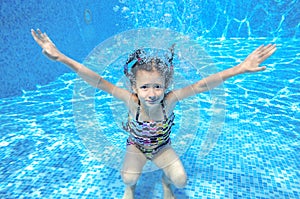 Happy girl swims in pool underwater, active kid swimming and having fun