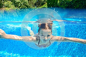 Happy girl swims in pool underwater, active kid swimming and having fun