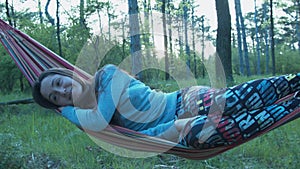 Happy girl swinging on a hammock in the park. Beautiful young woman smiling lying on a hammock.