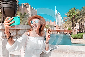 Happy girl takes a photo on her smartphone against the backdrop of the cityscape in Dubai with the hotel Burj al Arab photo