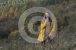 Happy girl takes pictures on smartphone of beautiful autumn forest. Young woman uses smartphone while walking in nature